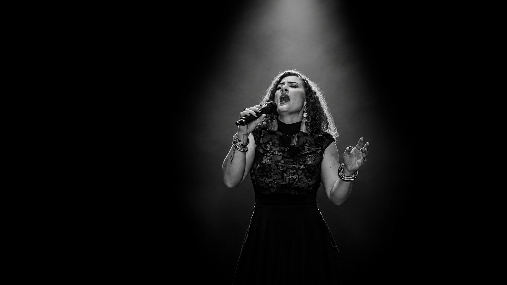 René Hunter singing into a microphone under a single stage spotlight